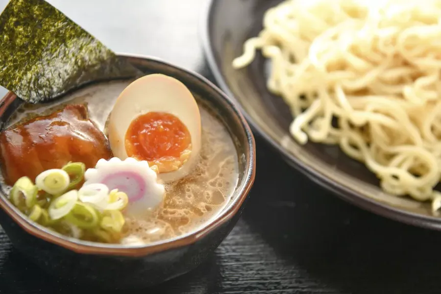 Primer plano de un plato de fideos y un plato de sopa de ramen con un huevo escalfado, cortado por la mitad.